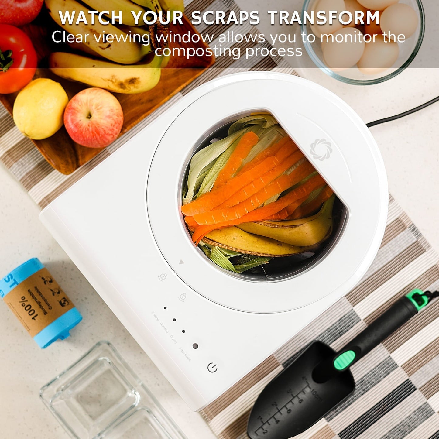 White Airthereal electric kitchen composting bin with food scraps on a kitchen counter, surrounded by fruits and a trowel.
