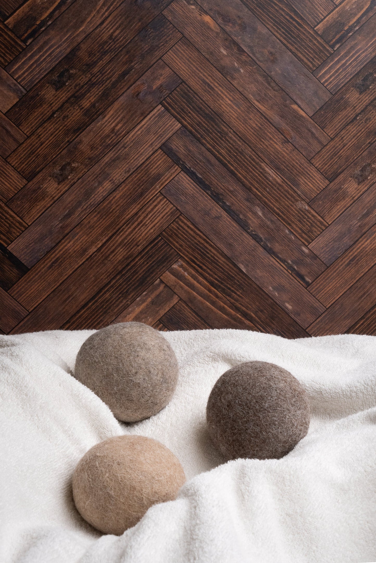 Three alpaca dryer balls on a white surface with a wooden herringbone pattern in the background