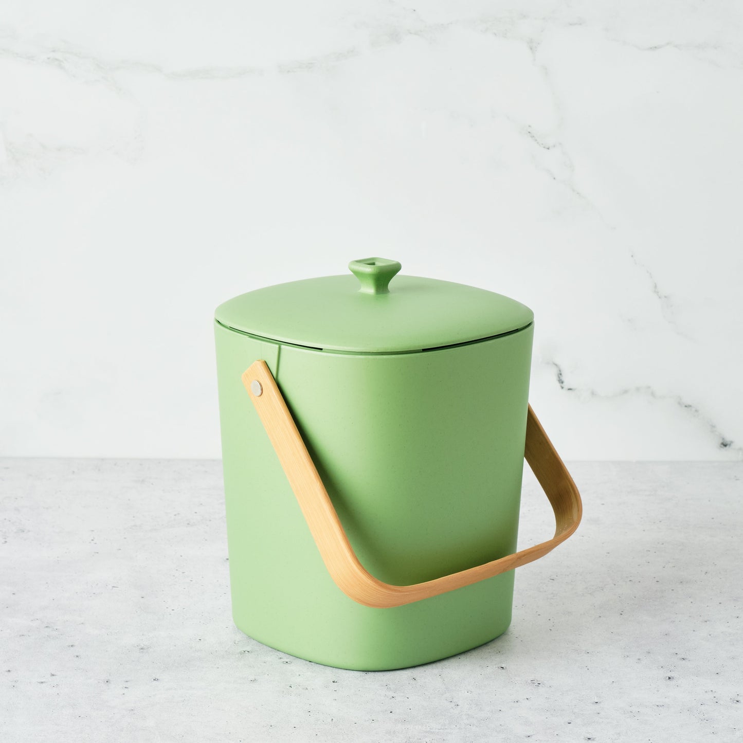 Avocado-colored Astrik Compoast Bin made of 100% biodegradable plant-based plastic with a bamboo handle on a light gray background.