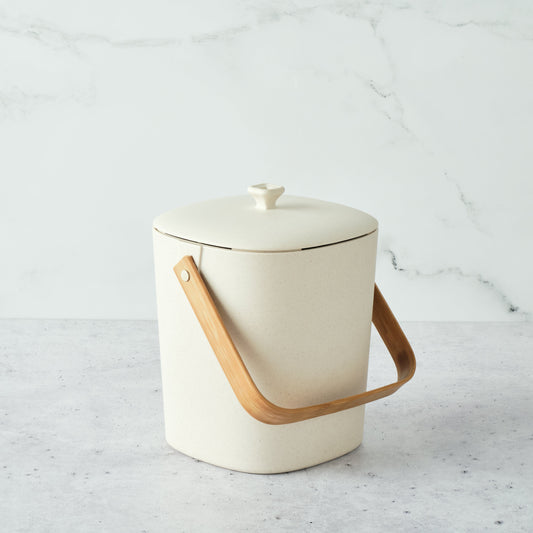 Natural-colored Astrik Compoast Bin made of 100% biodegradable plant-based plastic with a bamboo handle on a light gray background.