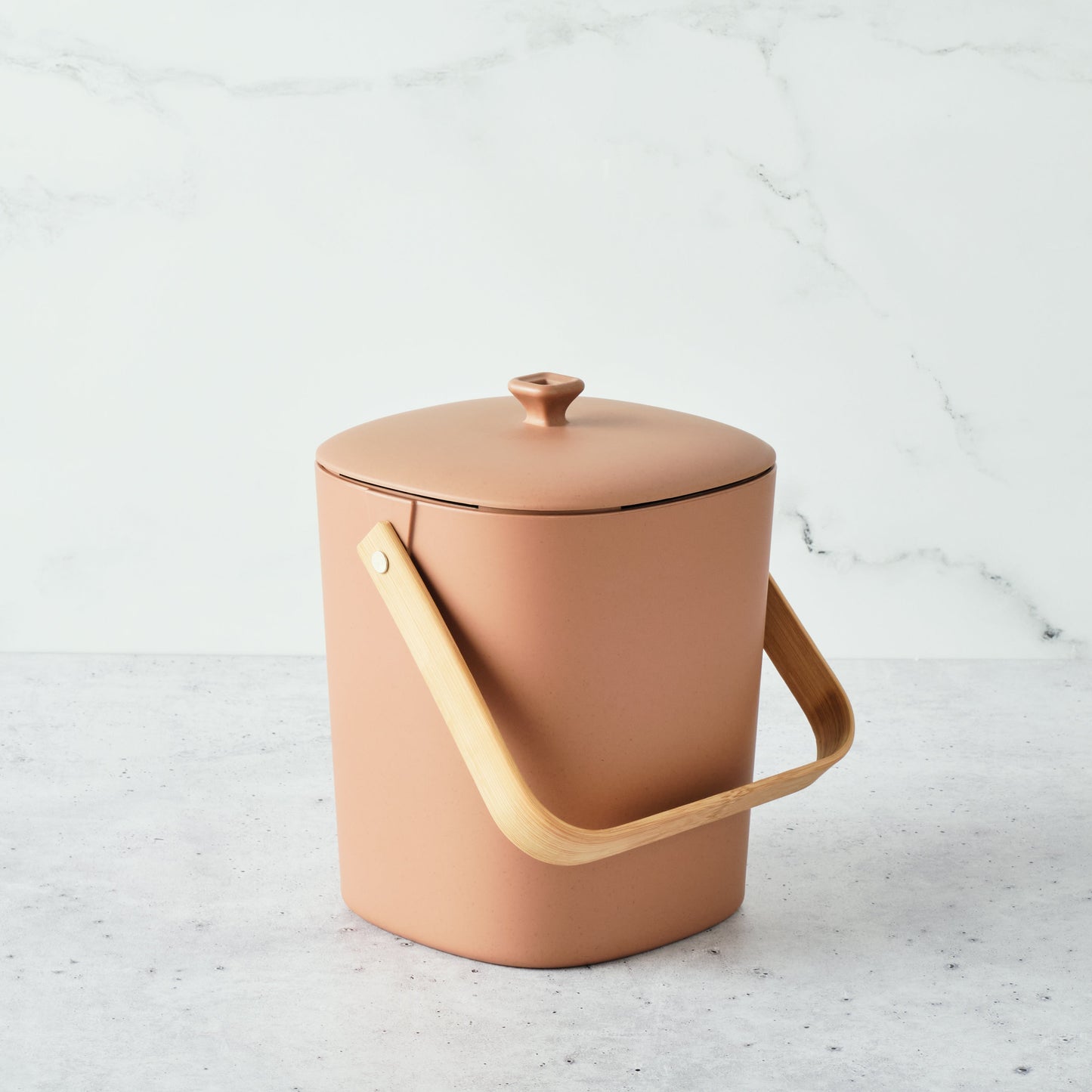 Terracotta-colored Astrik Compoast Bin made of 100% biodegradable plant-based plastic with a bamboo handle on a light gray background.
