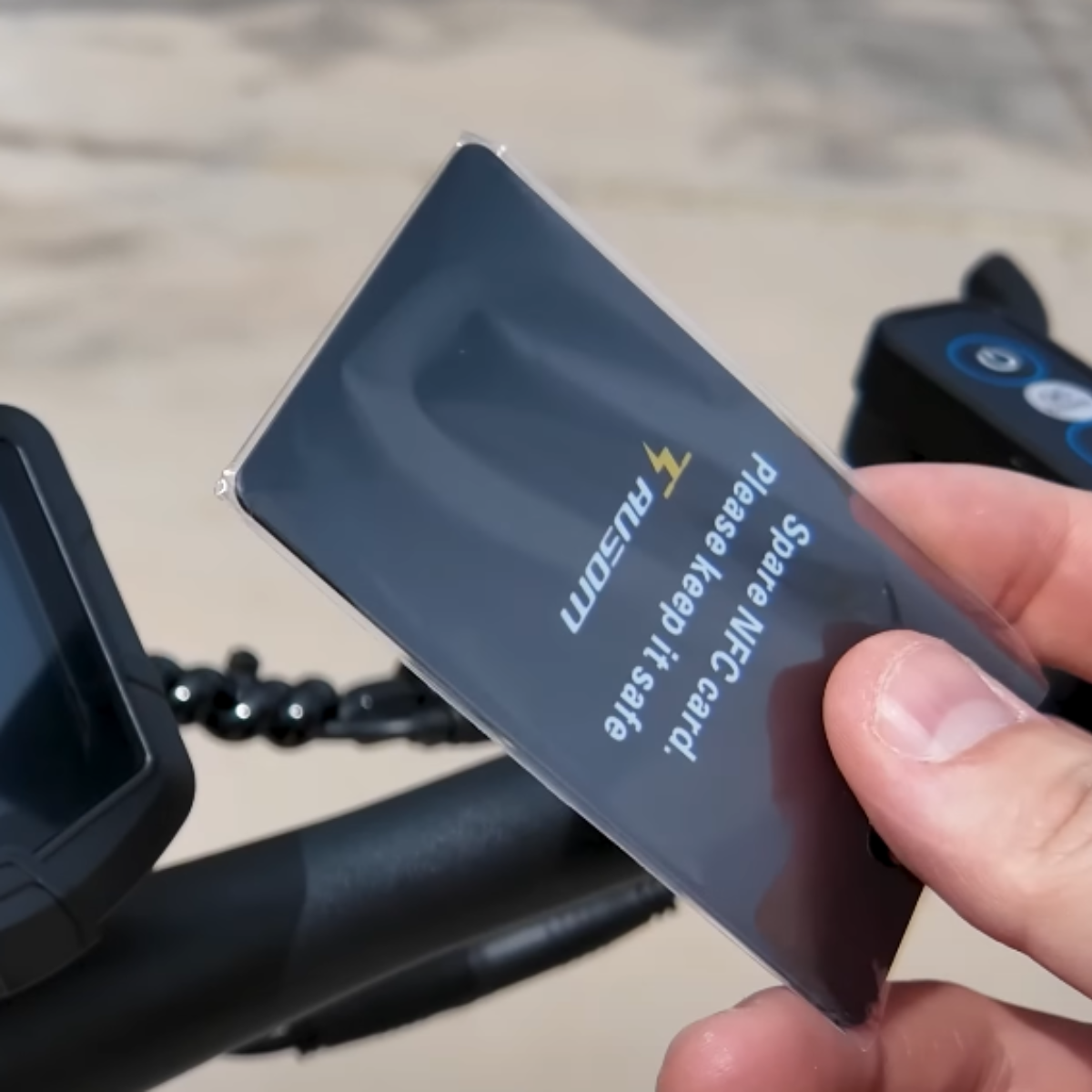 Person holding a spare NFC card for an AUSUM F1 Max electric scooter with a brand logo in an outdoor setting