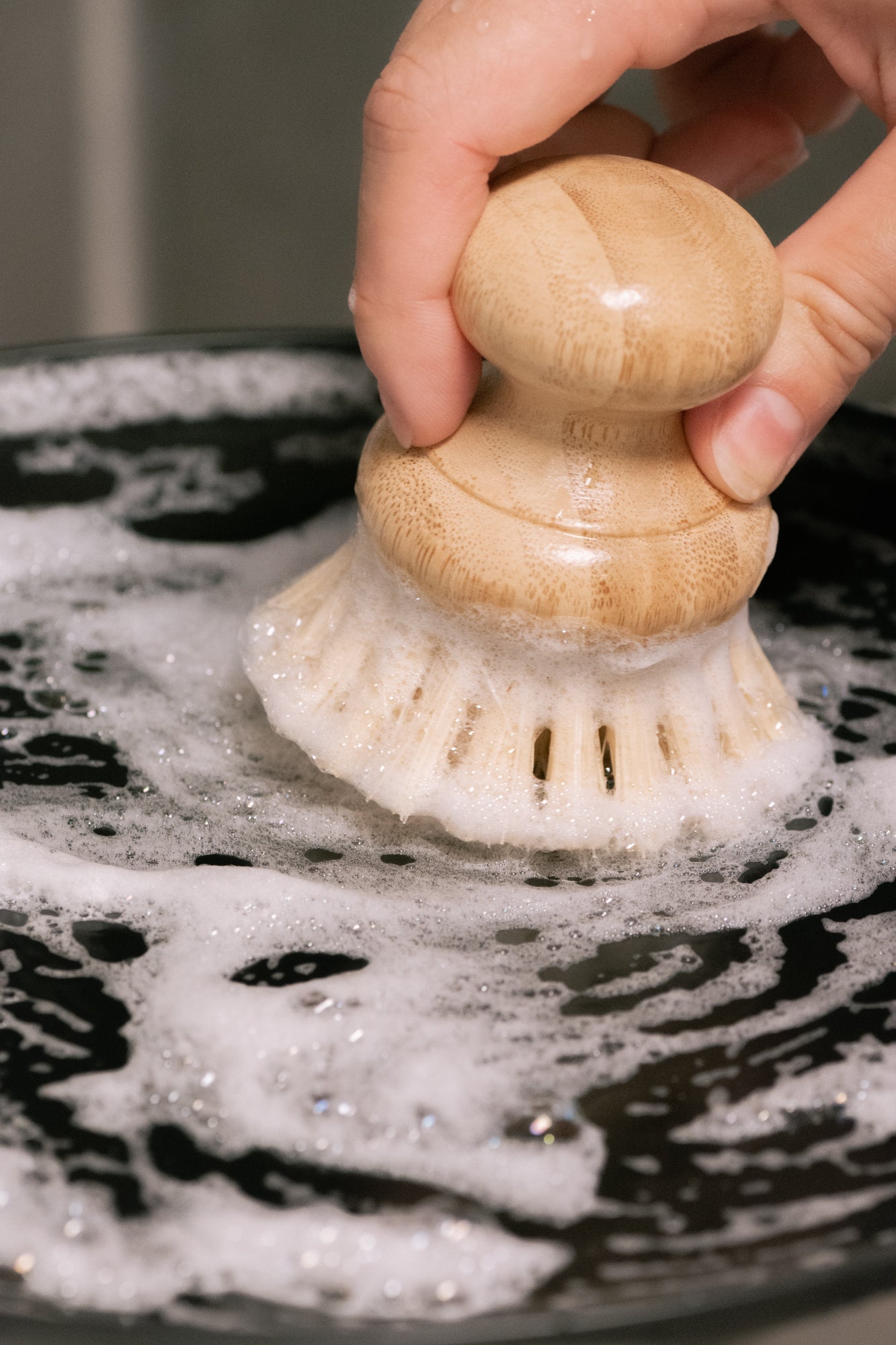 Hand using a scrubber on a soapy surface, made of No Tox Life Biodegradable Dish Block