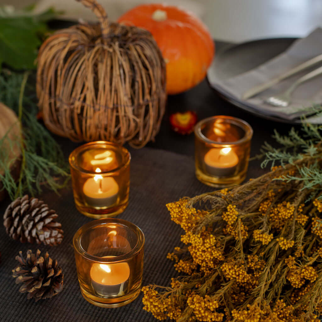 Autumn-themed table setting with Bluecorn Pure Beeswax Tea Light candles, pumpkins, and decorative elements on a dark surface.