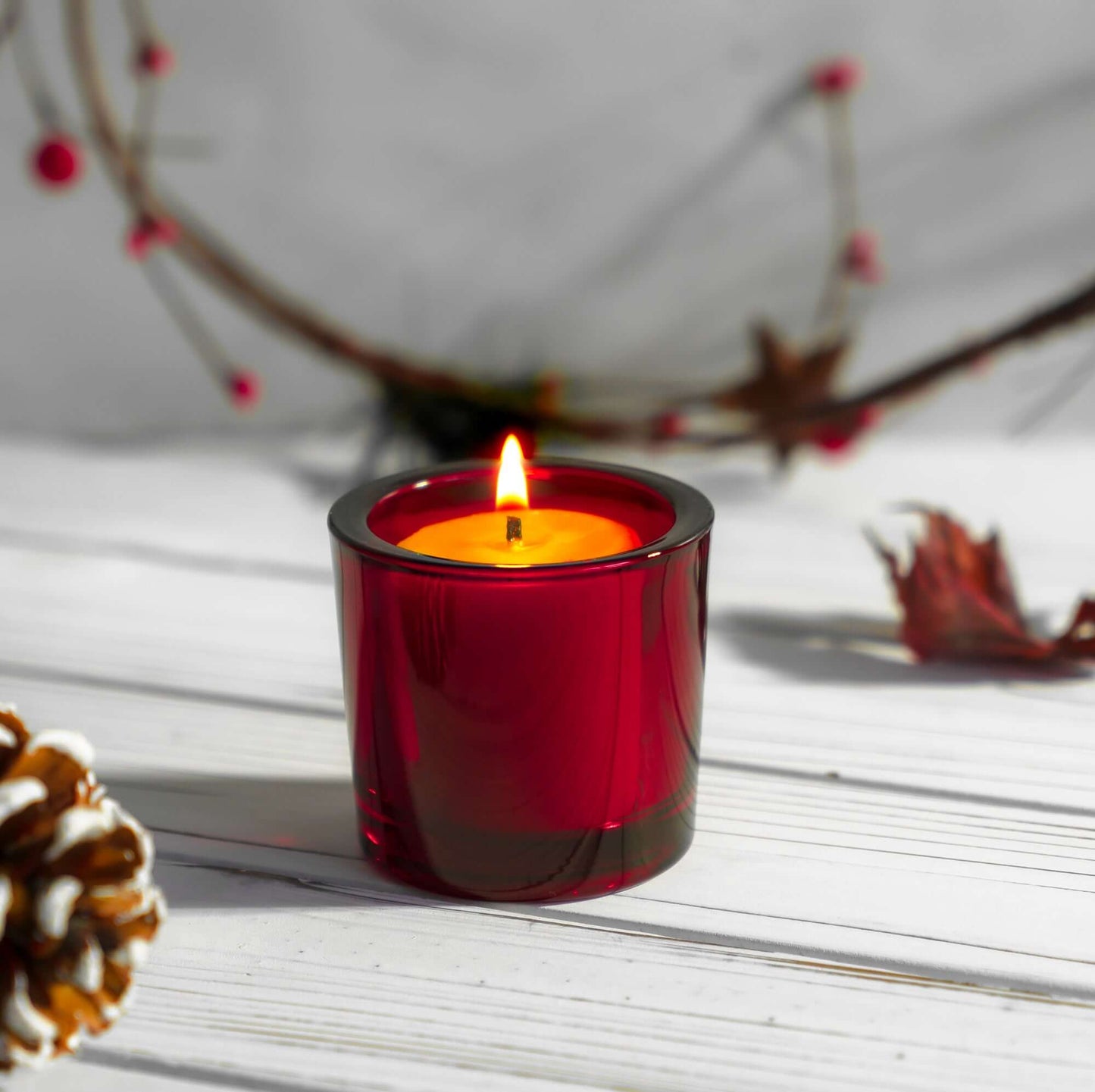 Red candle in a glass holder on a wooden surface with decorative elements.