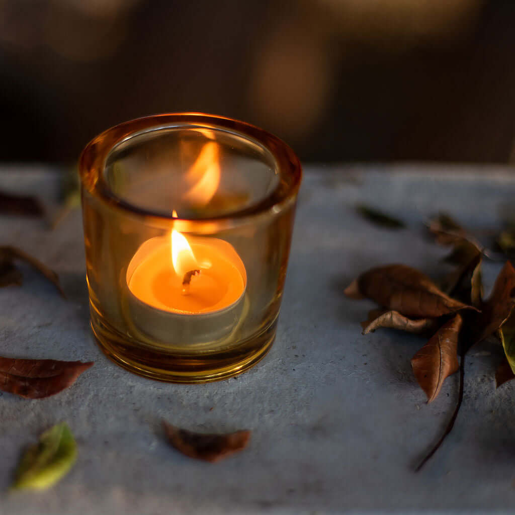 Small lit candle in a glass holder on a stone surface with leaves.
