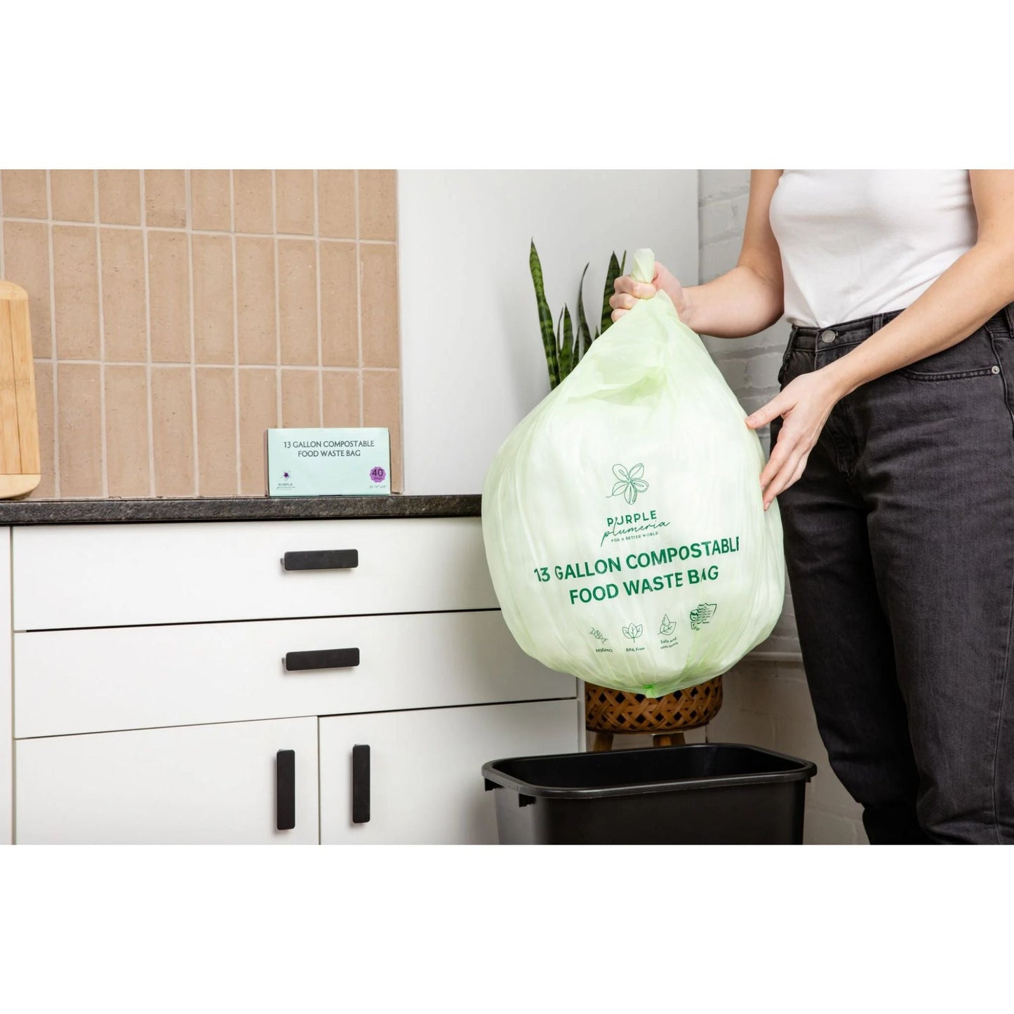 Person holding a green 13-gallon compostable food waste bag in a kitchen.