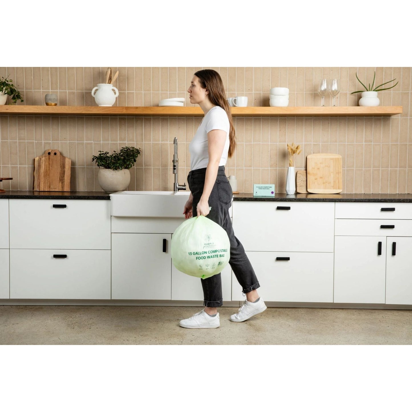 Person holding a compostable 13-gallon food waste bin in a kitchen.