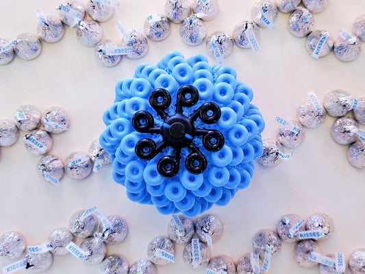Blue and black Cora Ball surrounded by silver and white wrapped candies on a light background.