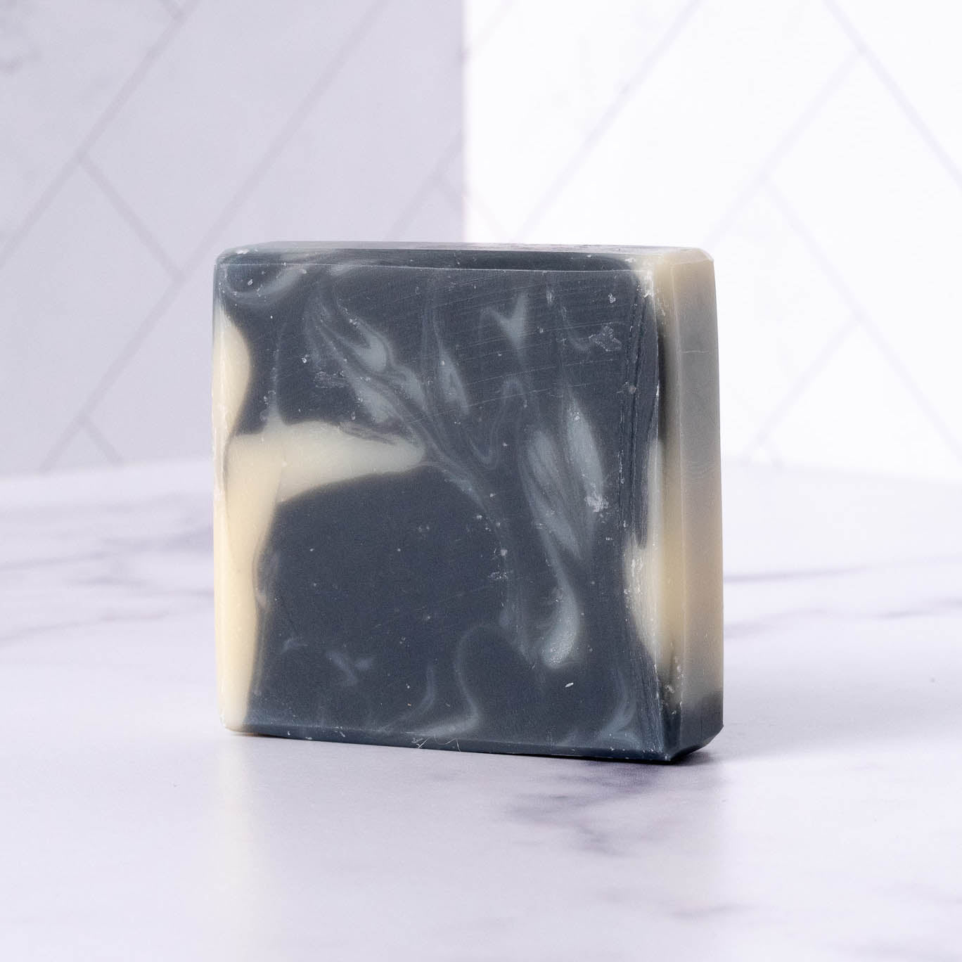 Bar of charcoal soap with black and white swirl pattern on a light gray background