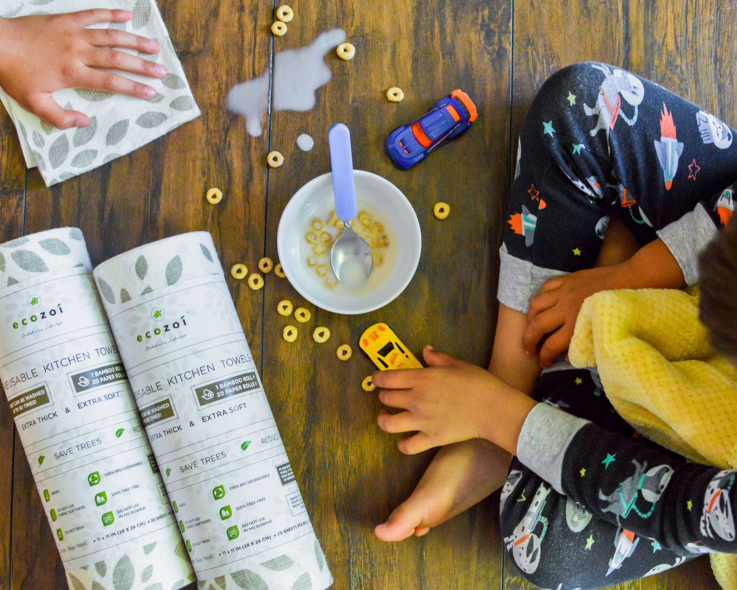 Children playing with toys on a wooden floor next to eco-friendly ecozoi reusable bamboo kitchen towels and cereal.