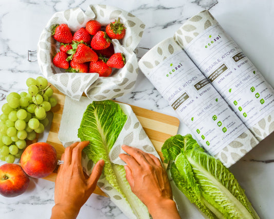 Person using eco-friendly bamboo reusable paper towels to wrap food on a marble countertop with fruits and vegetables.