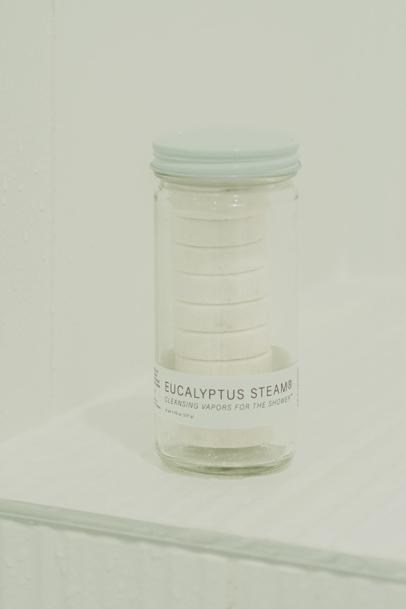 Clear glass full of eucalyptus steam shower vapors with a white lid on a white background