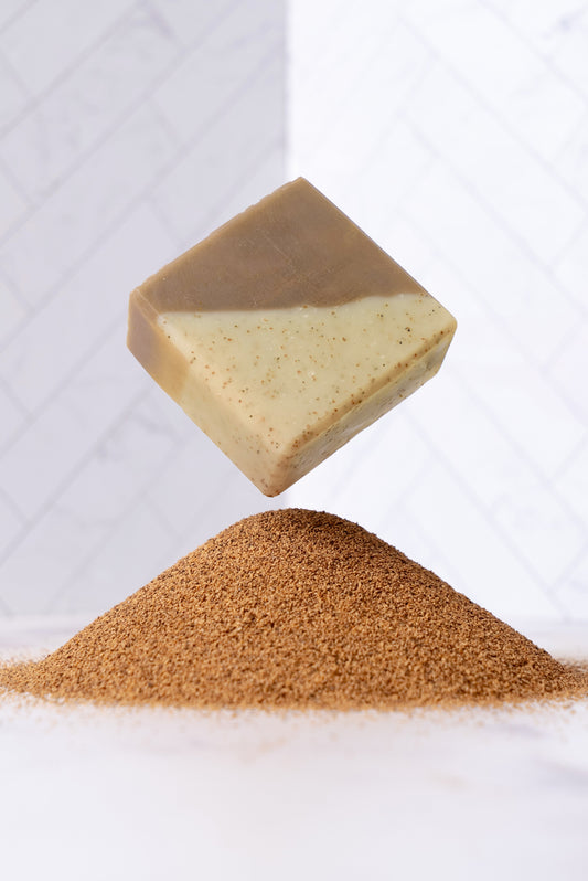 Bar of sandalwood patchouli soap with a pile of crushed walnut shells on a white background