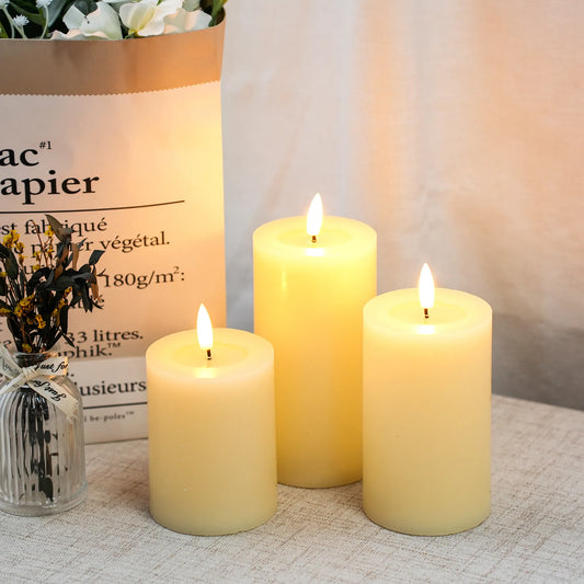 Three lit flameless LED candles on a textured surface with a bag and flowers in the background