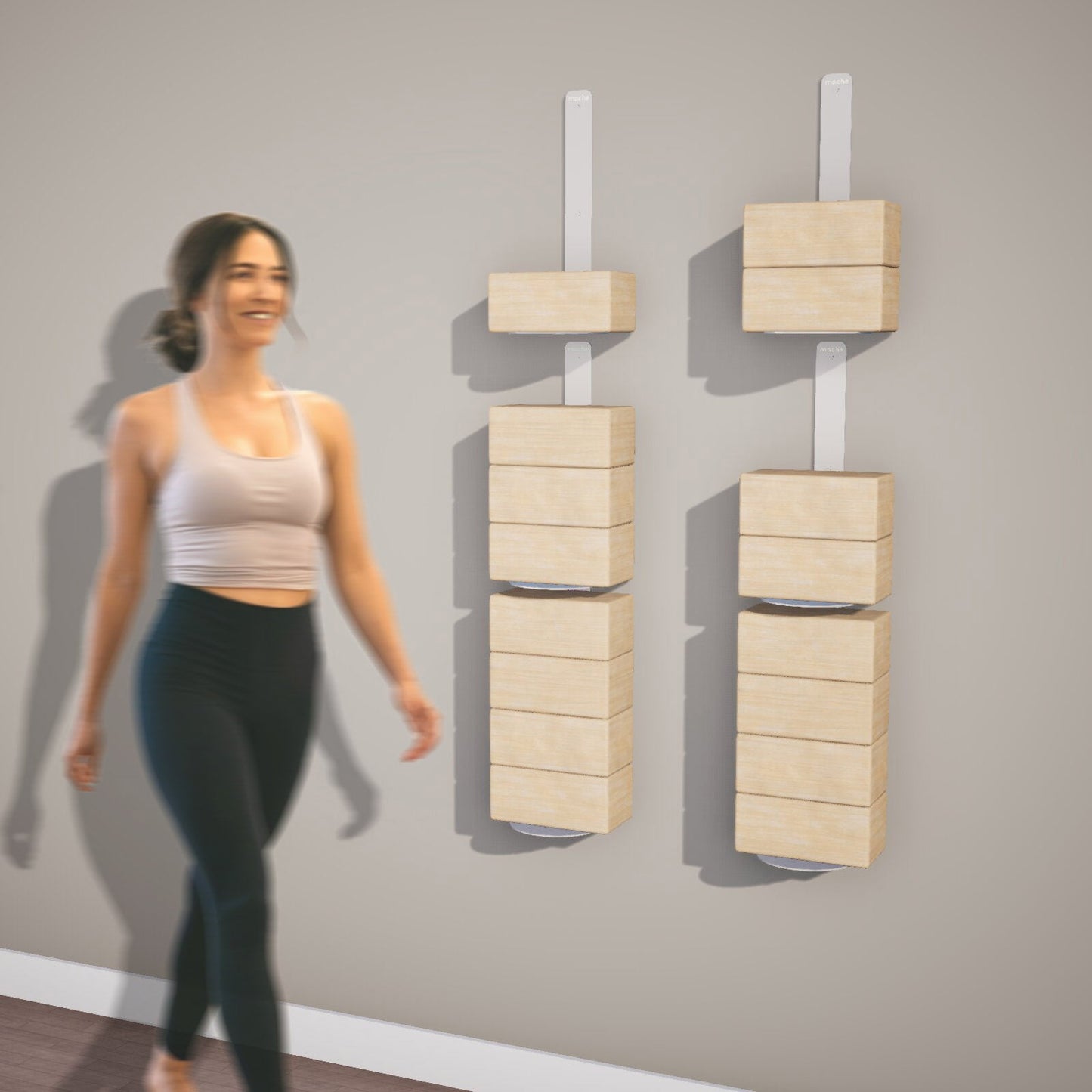 Woman standing next to multiple floating yoga block shelves on a gray wall with wooden yoga blocks on them.