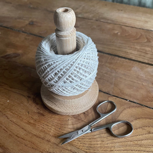 Oak spool with white string and a pair of scissors on a wooden surface