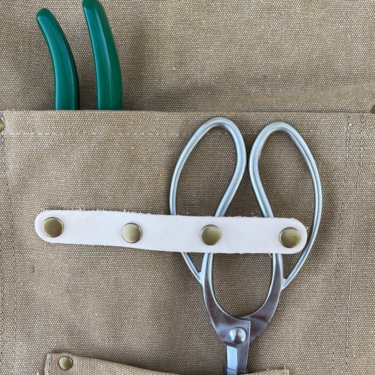 Shears and green-handled pliers in a beige tool pouch on a beige background