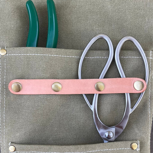 Leather strap with metal studs on a gray garden apron.