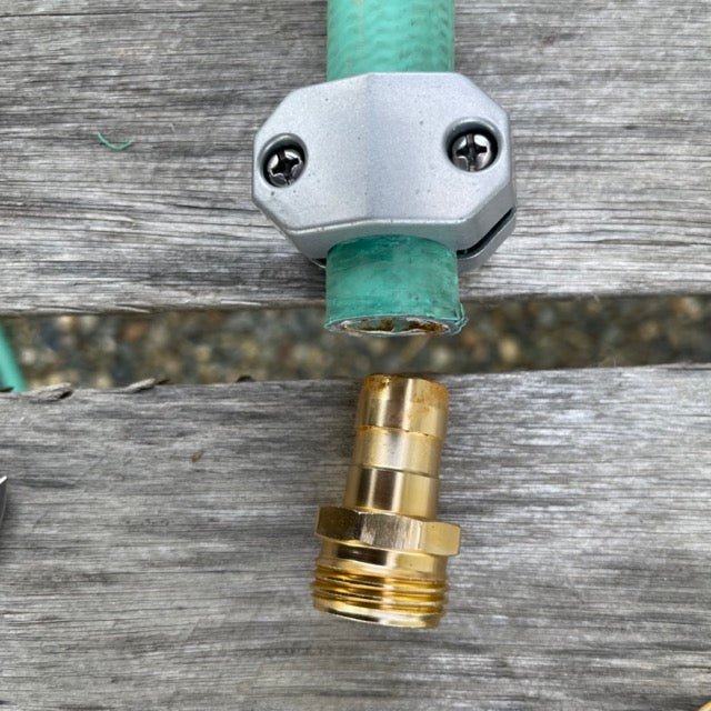 Green garden hose with a silver connector on a wooden surface, with a gold fitting in the foreground.