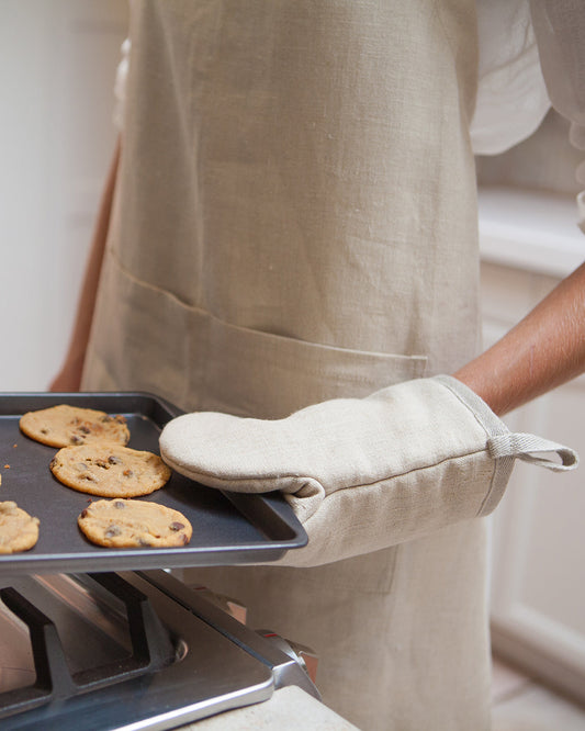 Person wearing a hemp apron and hemp oven mitt by Hemptique, holding a tray of cookies.