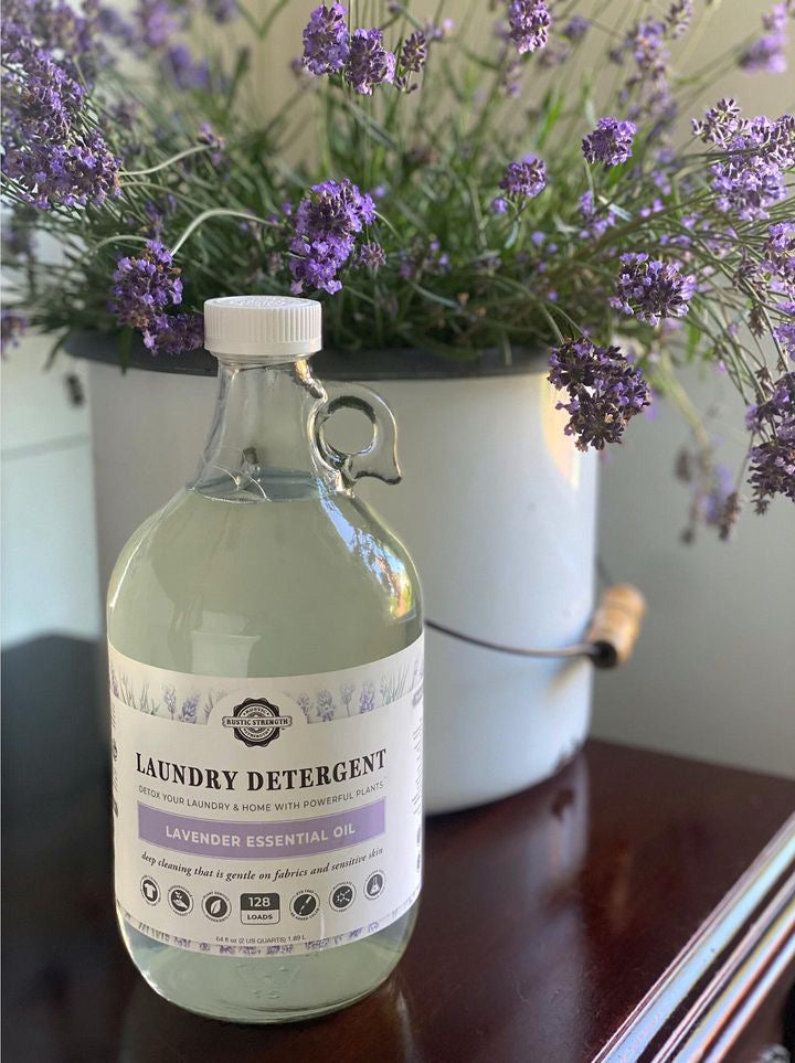 Bottle of Rustic Strength lavender essential oil laundry detergent with a vase of lavender flowers in the background.