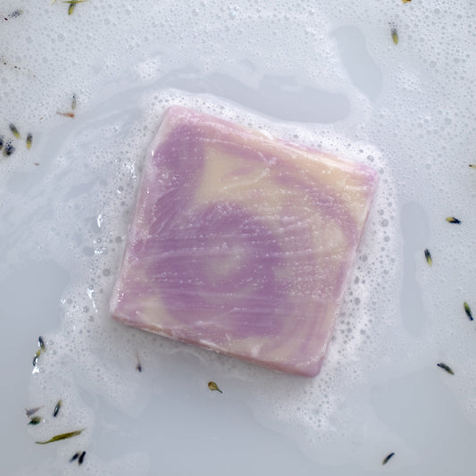 Purple and white lavender soap bar on a soapy surface with lavender flowers.