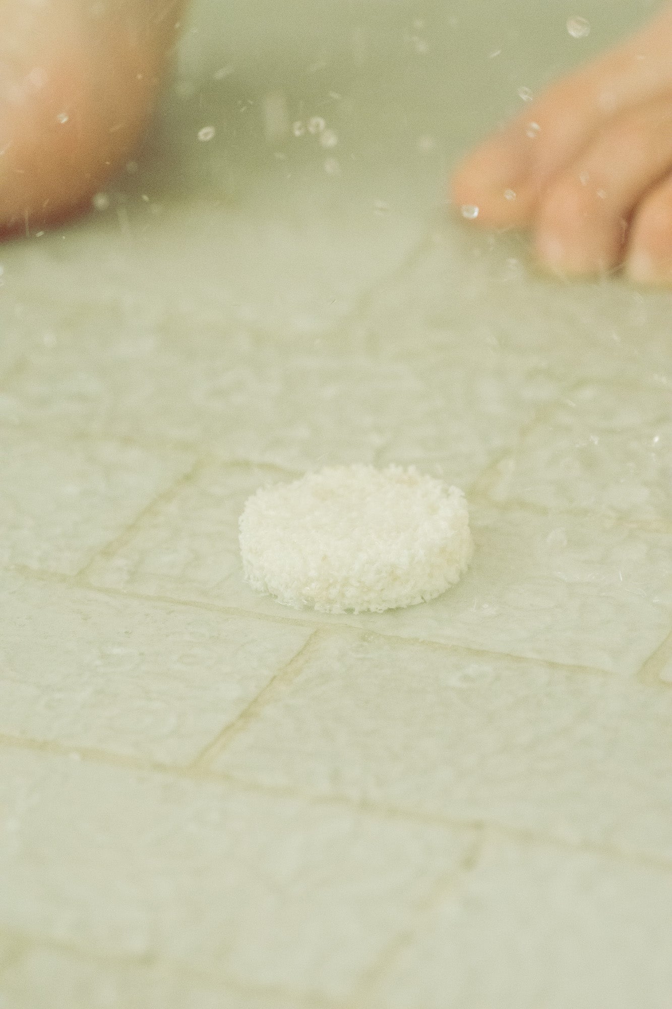 Close-up of a white eucalyptus steam shower vapor on a textured green tiled surface with blurred feet in the background