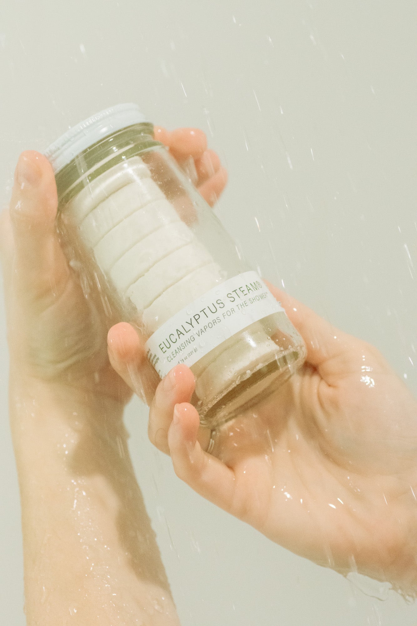 Hand holding a glass bottle labeled 'Eucalyptus Steam' against a light background