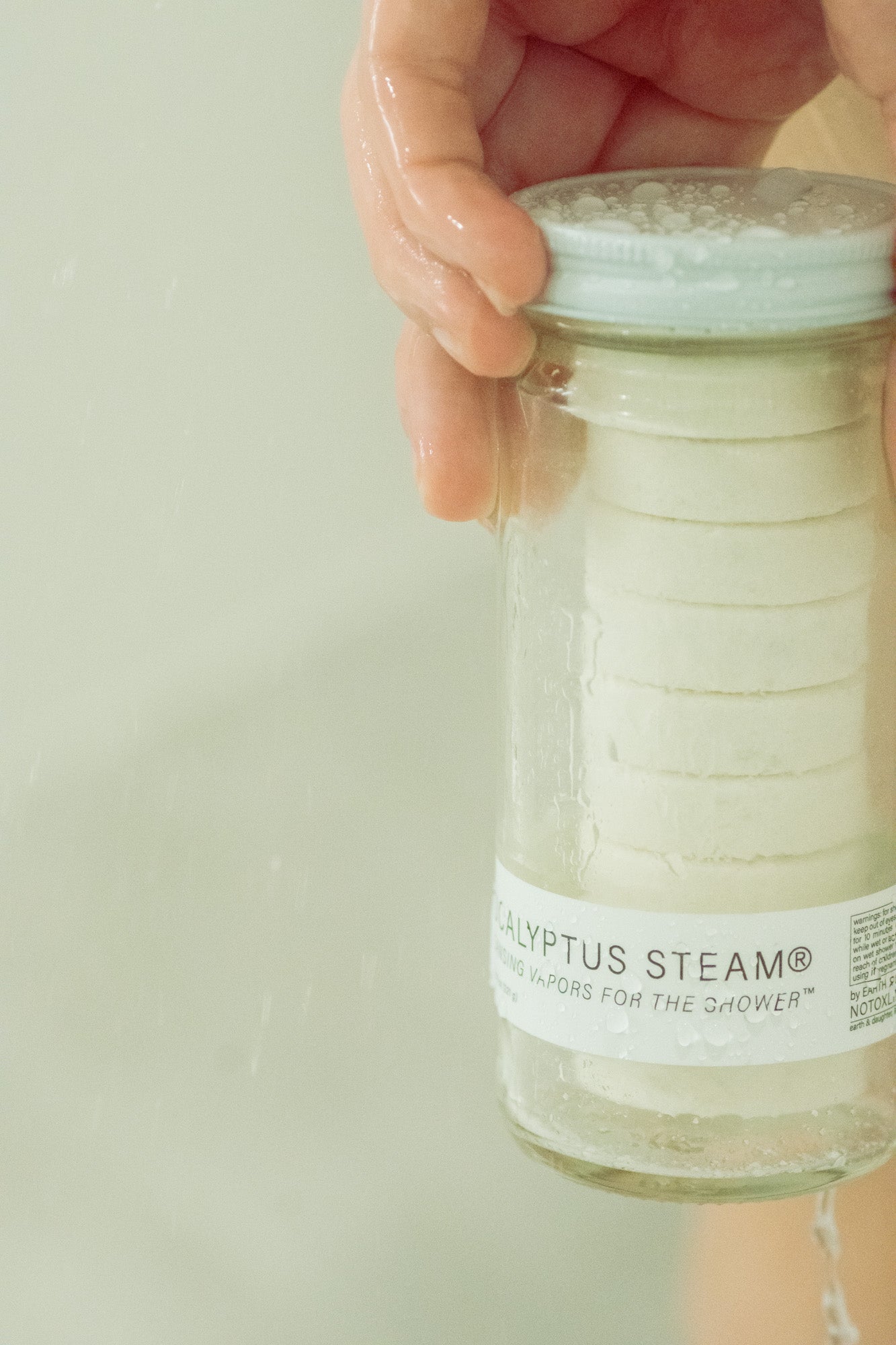 Hand holding a jar of Eucalyptus Steam Shower Vapors against a neutral background