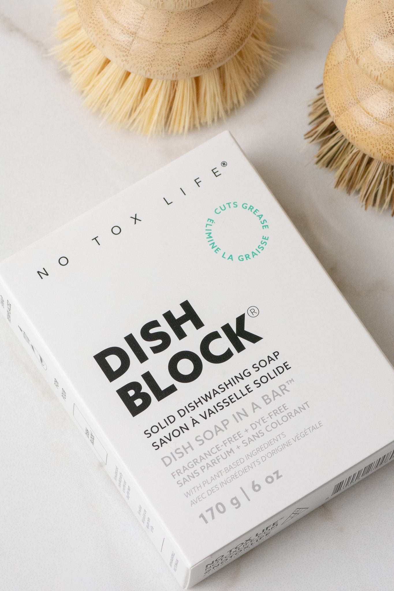 No Tox Life Dish Block solid dishwashing soap on a white surface with brushes in the background