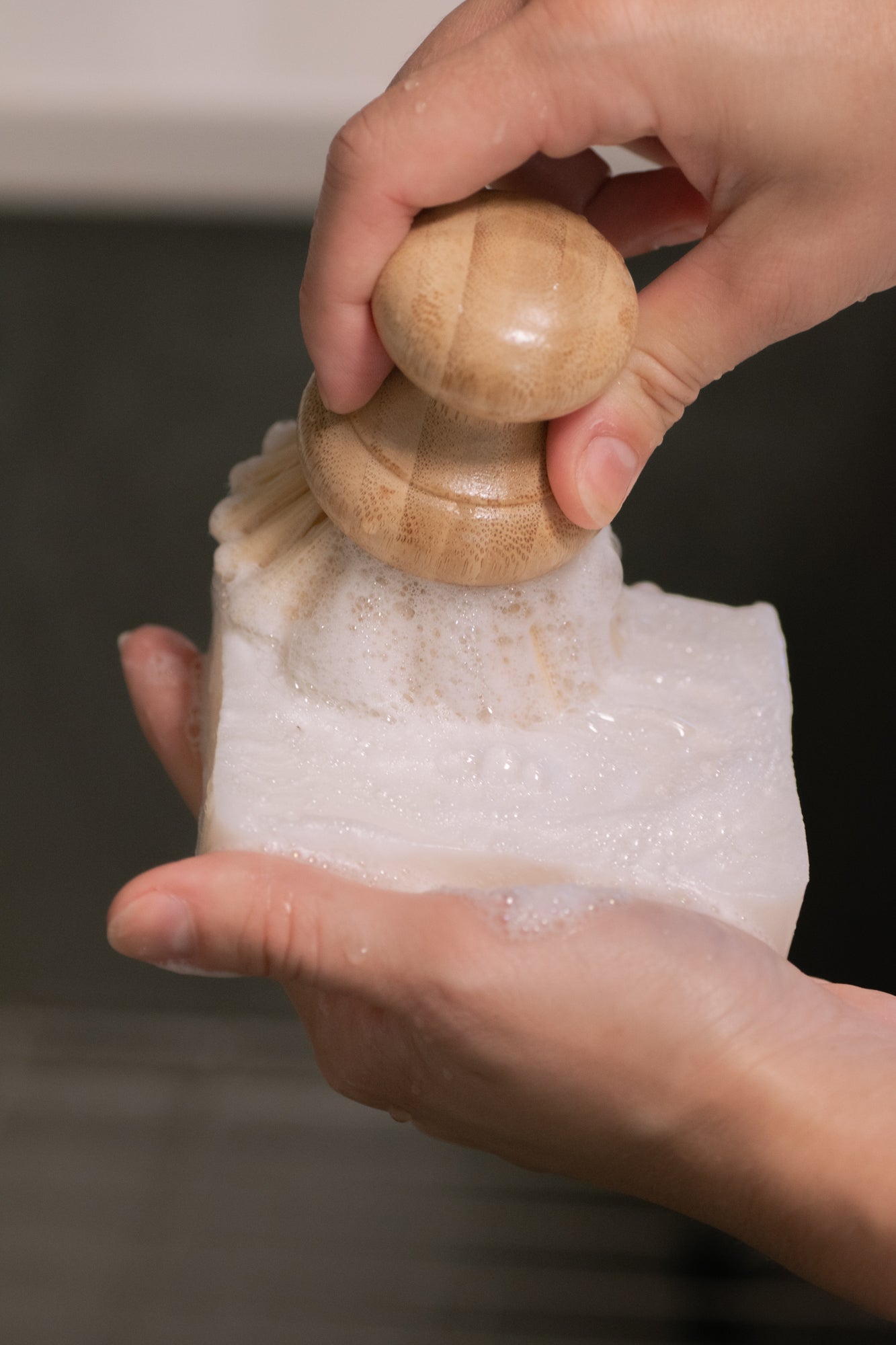 Hand holding a wooden scrub brush on a sudsyNo Tox Life Zero-Waste Dish Block