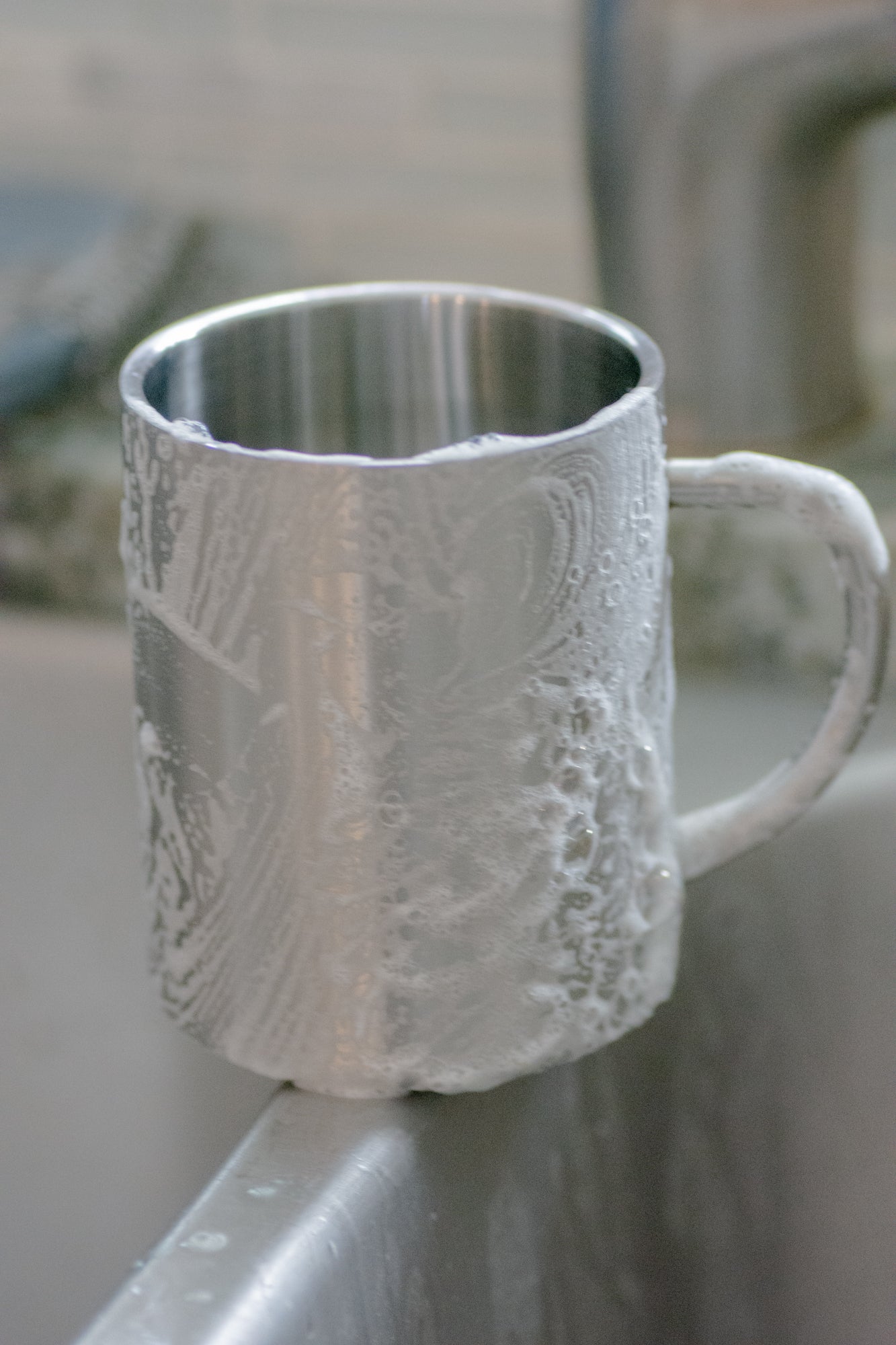 Metallic mug with soap suds from No Tox Life Dish Block surface on a neutral background
