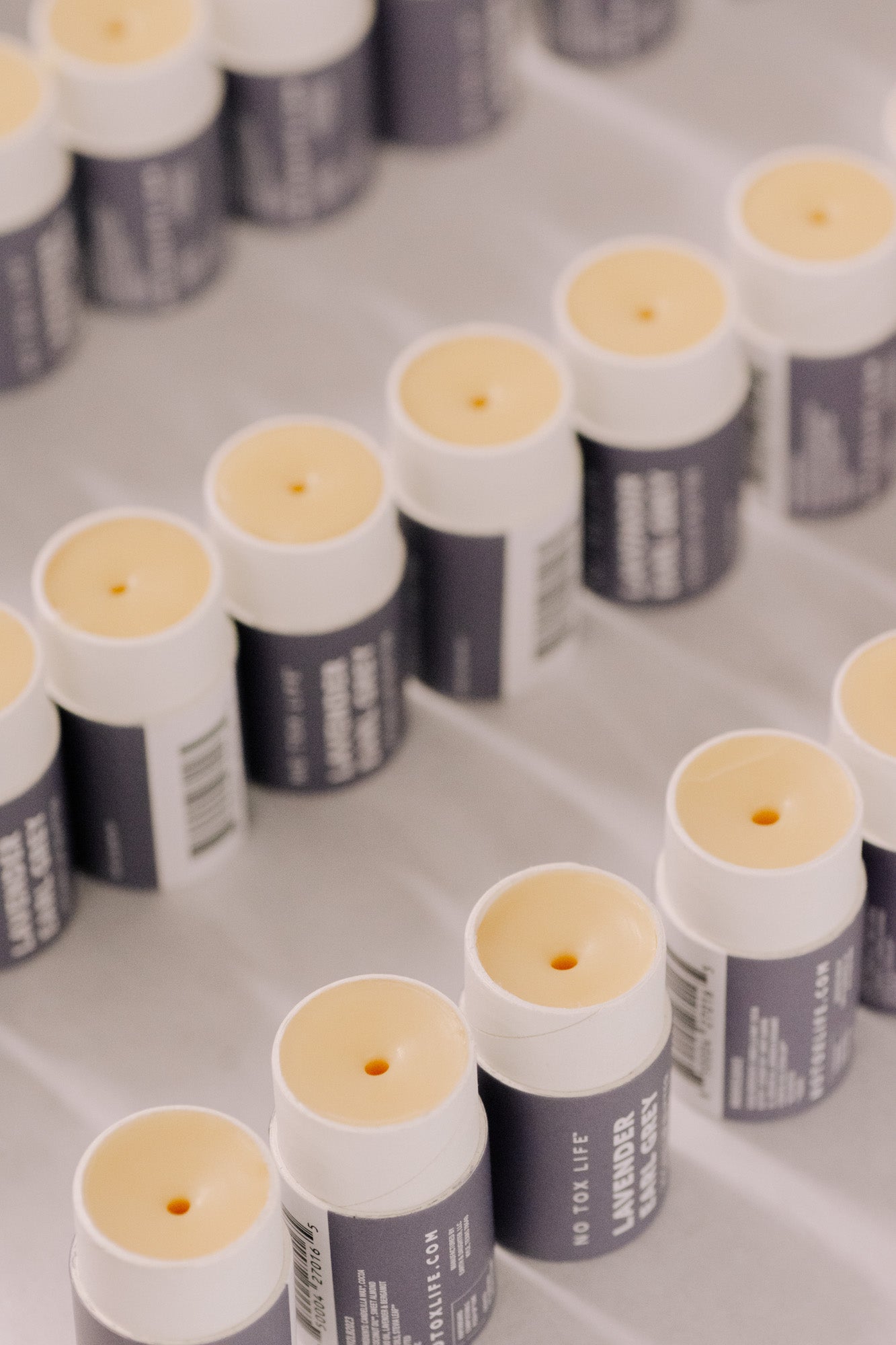 Multiple tubes of No Tox Life SolidSilk Lavender Earl Grey lip balm tubes on a reflective surface