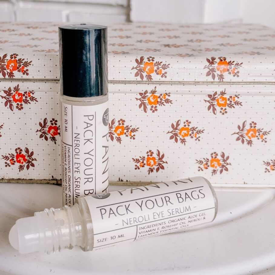 Roll-on bottle of 'Pack Your Bags' Organic Neroli Eye Serum by Pantry with floral-patterned box in the background. Vegan, Vegetarian, Gluten-Free, Cruelty-Free eye serum
