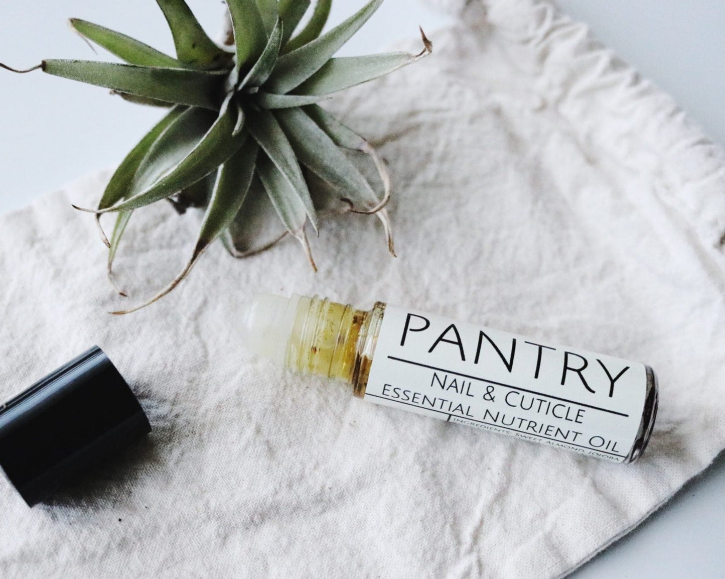 Pantry nail and cuticle essential nutrient oil roll-on bottle on a white linen with a plant in the background