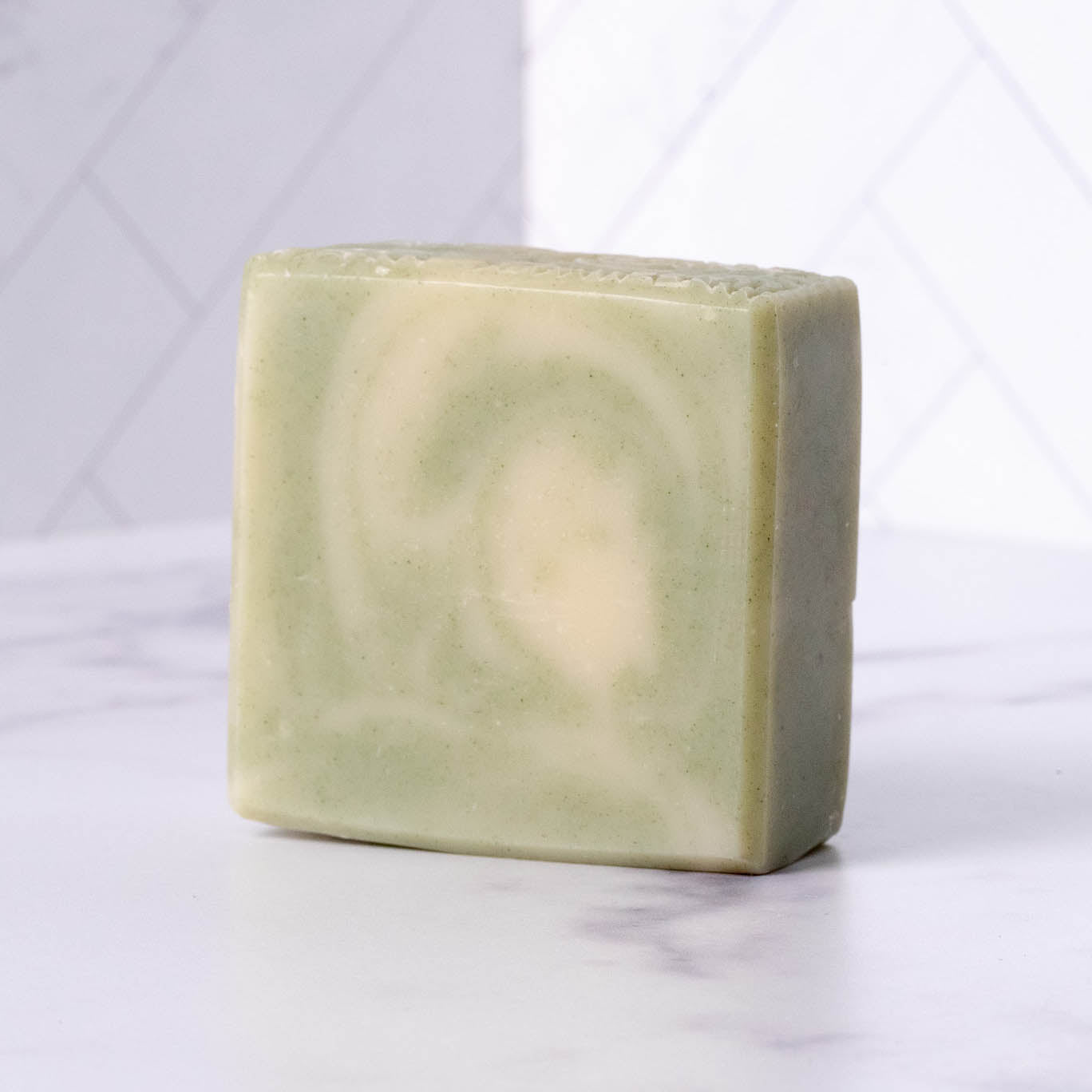 Green and white peppermint tea tree soap bar on a white marble surface