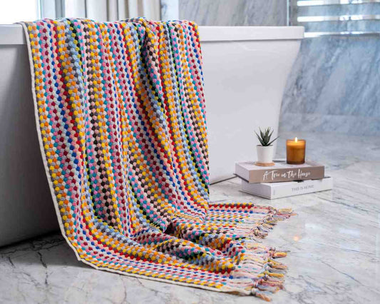 Colorful textured Premium Organic Turkish Jacquard Bath Towel draped over a bathtub with a candle and book on a marble surface.