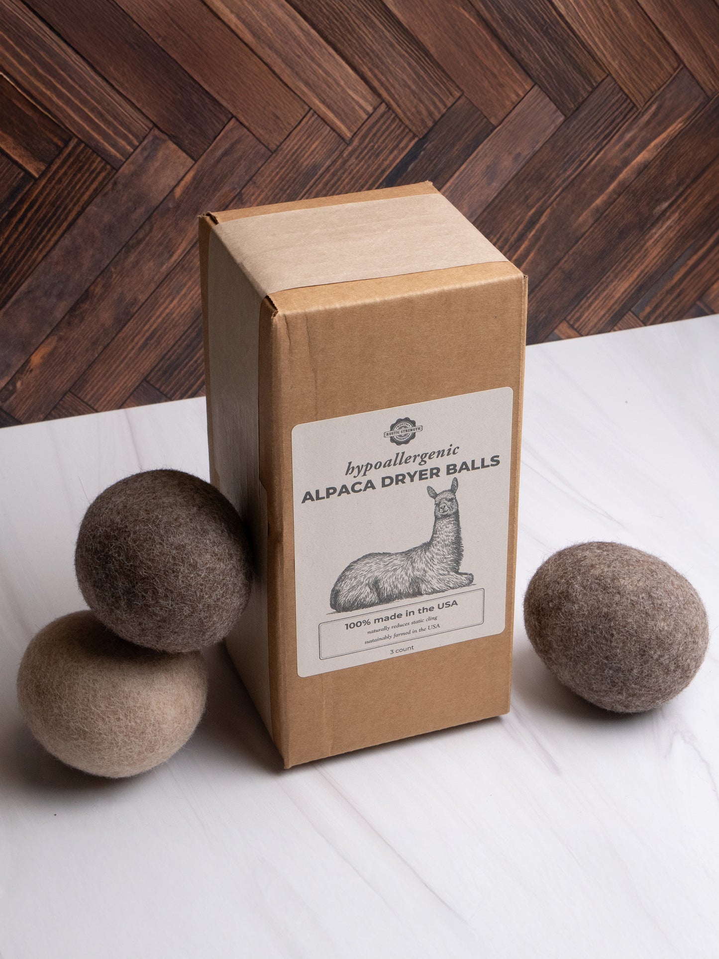 Box of hypoallergenic rustic strength alpaca dryer balls with three balls on a white sheet on a wooden floor.