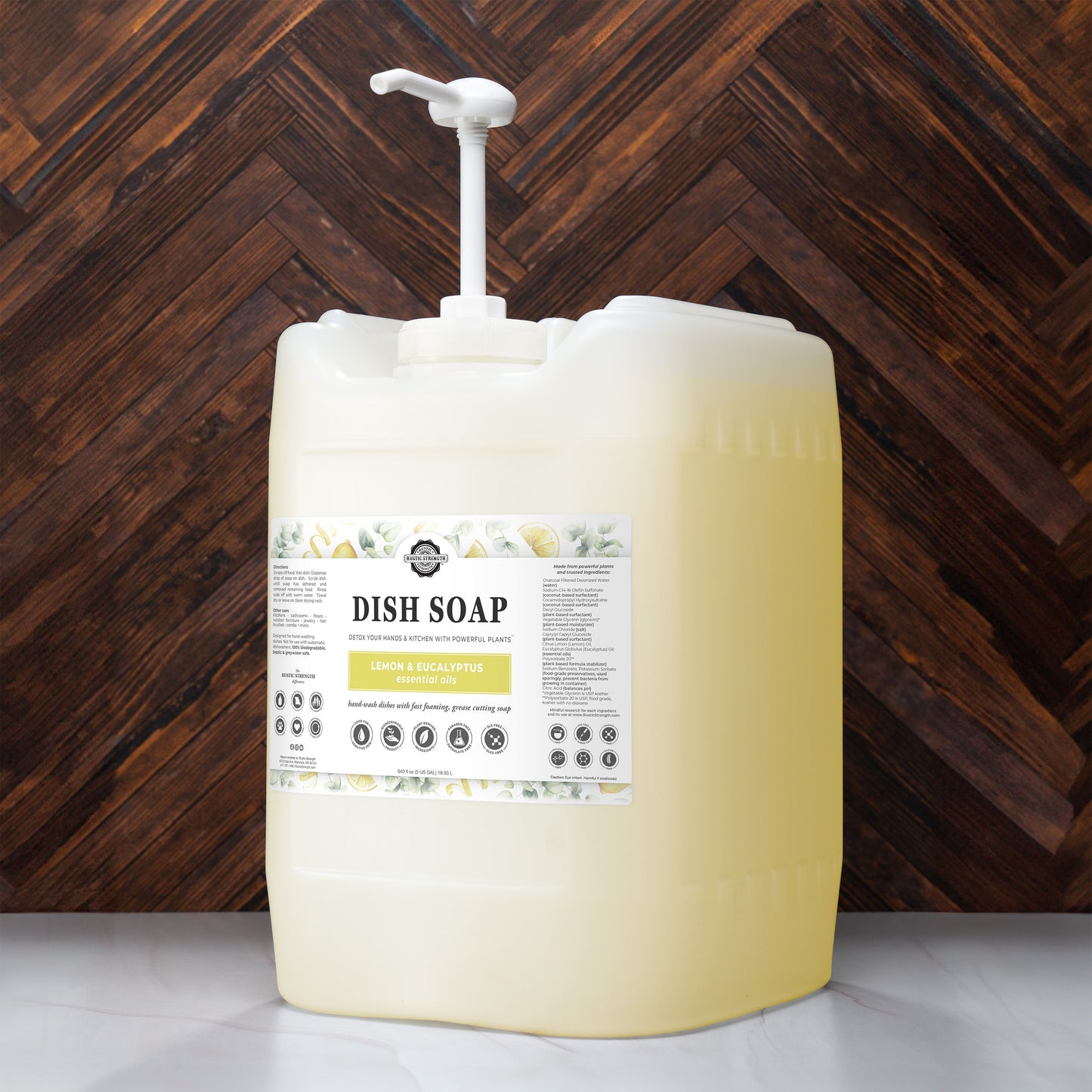 5 gallon container of Rustic Strength Lemon & Eucalyptus Dish Soap with a pump against a wooden background