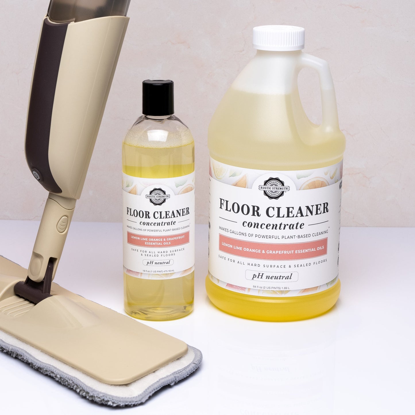 Two bottles of Rustic Strength floor cleaner and a cleaning mop on a white surface.