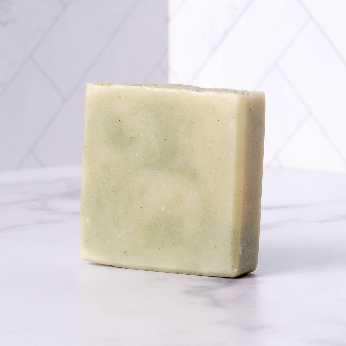 Square bar of peppermint tea tree soap on a white marble surface with a light gray geometric patterned background