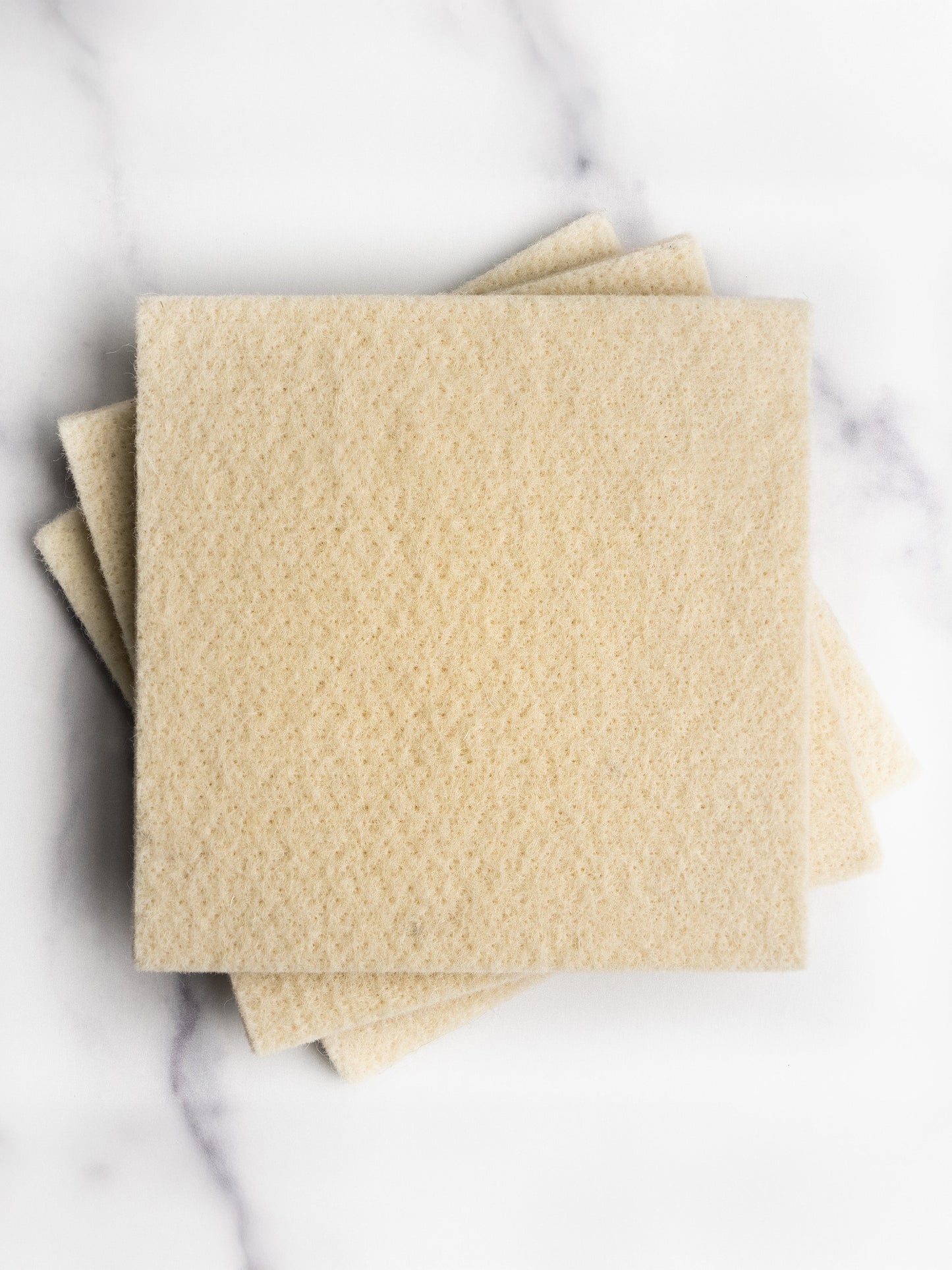 Three beige wool sponges on a marble surface