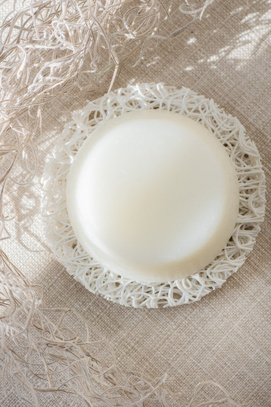 White shampoo and conditioner bar on a decorative lace doily with a textured beige background