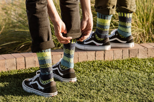 Two people wearing brown sneakers with Solmate Lemongrass Crew socks outdoors on grass.