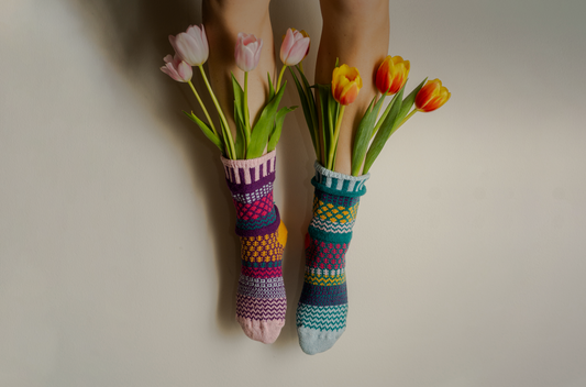 Solmate Petunia Crew Socks - Mismatched, colorful socks with tulips held in each foot against a neutral background