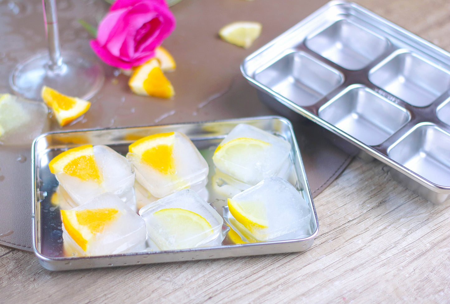 Stainless steel baking tray with lemon slices and ice cubes on a wooden surface.
