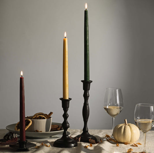 Decorative candles with candlesticks on a table with wine glasses and a pumpkin.