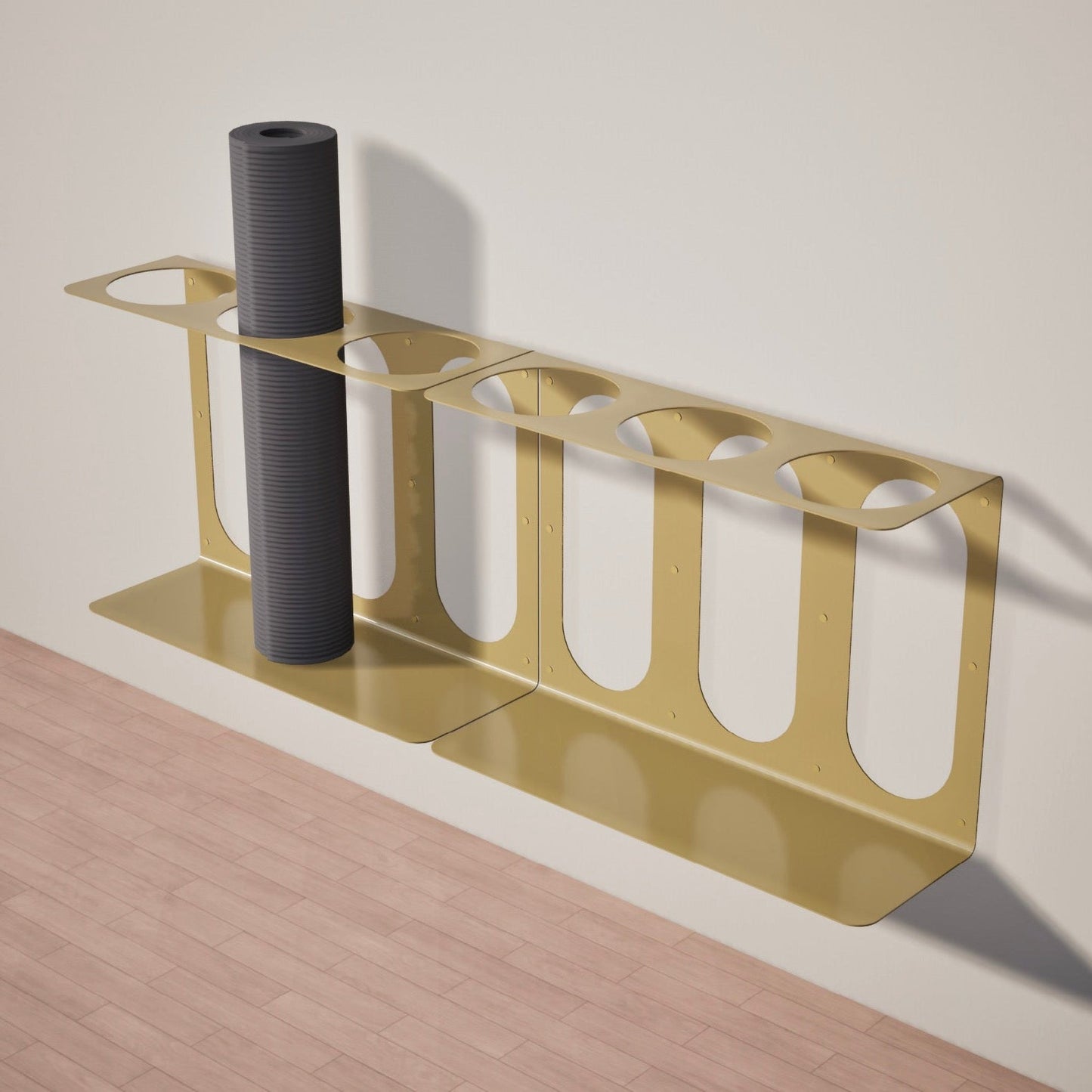 Two gold Yoke yoga mat wall brackets mounted side-by-side with a gray yoga mat on one of the 3 available slots, on a wooden floor against a beige wall