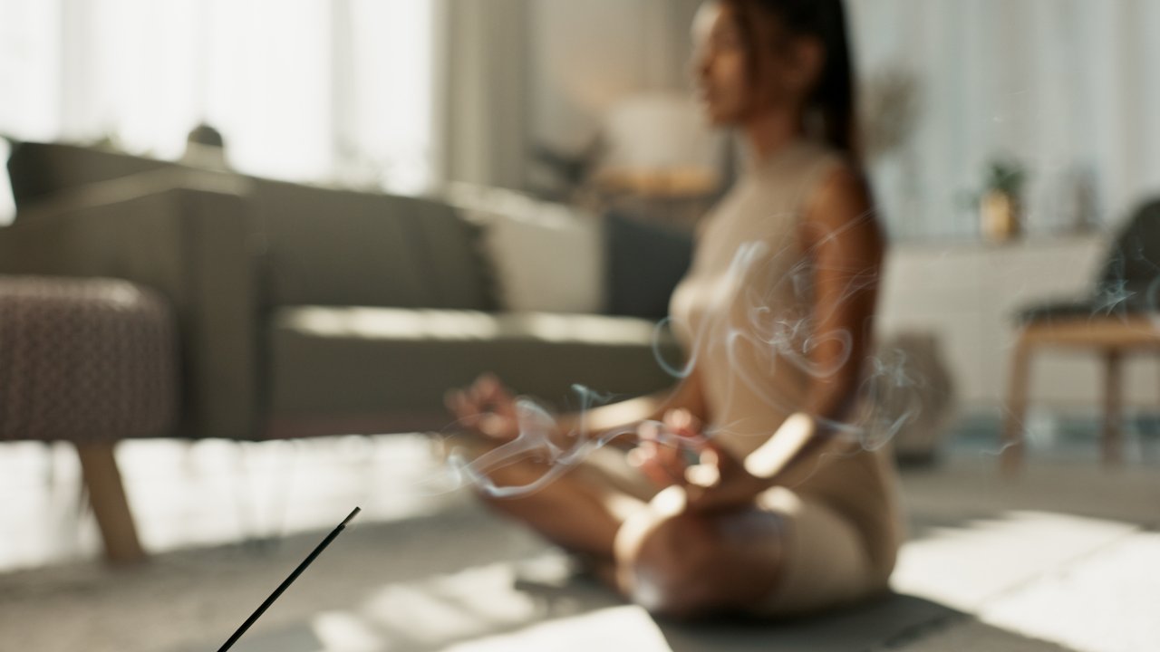 Woman meditating on living room floor with incense 